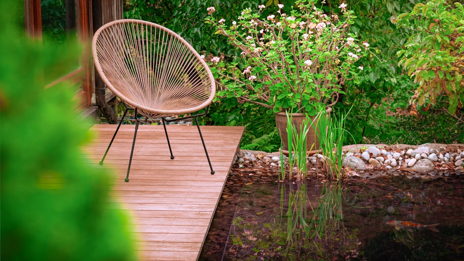 Tranquil garden patio with a stylish chair by a pond, surrounded by lush greenery.